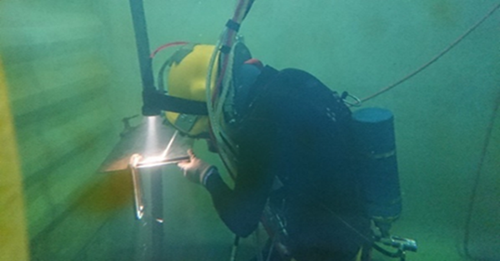 Trainees wearing surface-supplied diving equipment during underwater welding training.